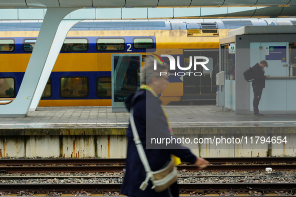 At Arnhem Centraal train station's platform in Arnhem, Netherlands, on July 27, 2023, a woman walks by while another commuter checks his pho...