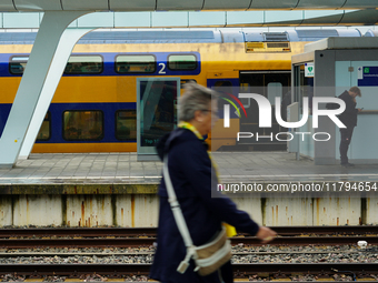 At Arnhem Centraal train station's platform in Arnhem, Netherlands, on July 27, 2023, a woman walks by while another commuter checks his pho...