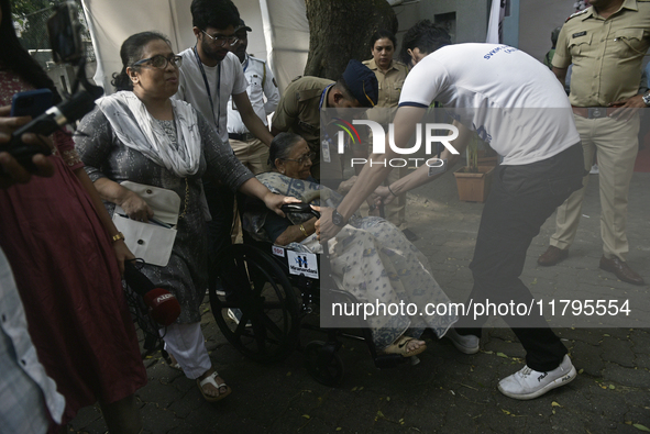 A volunteer helps pull a wheelchair for an elderly woman as she enters to cast her ballot during the Maharashtra state assembly elections at...