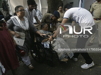 A volunteer helps pull a wheelchair for an elderly woman as she enters to cast her ballot during the Maharashtra state assembly elections at...