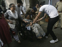 A volunteer helps pull a wheelchair for an elderly woman as she enters to cast her ballot during the Maharashtra state assembly elections at...