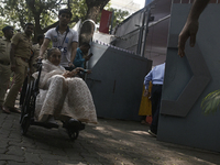 An old woman in a wheelchair comes out after casting her ballot to vote during the Maharashtra state assembly elections at a polling booth i...