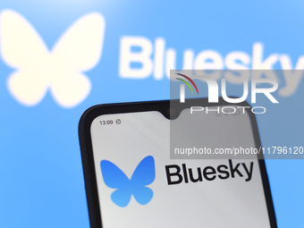 The logo of the social network Bluesky appears on the screen of a smartphone and on the computer screen in the background in Reno, United St...