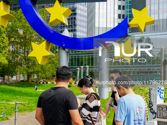 Visitors gather around the iconic 14-meter-high Euro sculpture by Ottmar Horl at Willy-Brandt-Platz in Frankfurt am Main, Germany, on August...