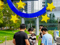 Visitors gather around the iconic 14-meter-high Euro sculpture by Ottmar Horl at Willy-Brandt-Platz in Frankfurt am Main, Germany, on August...