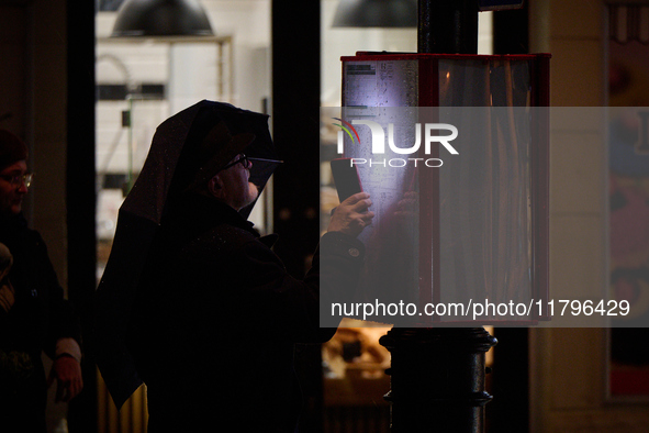 A man looks at a bus schedule witht he light of his mobile phone in Warsaw, Poland on 20 November, 2024. 