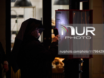 A man looks at a bus schedule witht he light of his mobile phone in Warsaw, Poland on 20 November, 2024. (