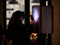 A man looks at a bus schedule witht he light of his mobile phone in Warsaw, Poland on 20 November, 2024. (