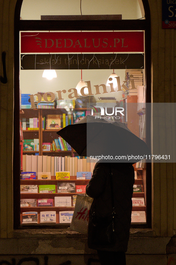 A woman with an umbrella is seen looking at a book shop window in Warsaw, Poland on 20 November, 2024. 