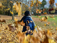 A woman throws colorful fallen leaves in the air during the autumn season in Toronto, Ontario, Canada, on November 6, 2024. (