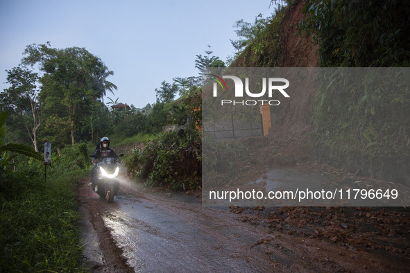 Residents on motorbikes cross a road section covered by landslide material after a flash flood and landslide hit Mekarbuana village, Karawan...