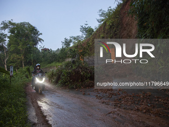 Residents on motorbikes cross a road section covered by landslide material after a flash flood and landslide hit Mekarbuana village, Karawan...