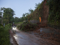 Residents on motorbikes cross a road section covered by landslide material after a flash flood and landslide hit Mekarbuana village, Karawan...