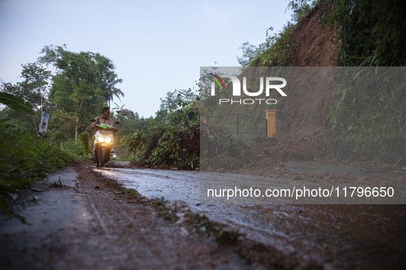 Residents on motorbikes cross a road section covered by landslide material after a flash flood and landslide hit Mekarbuana village, Karawan...