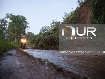 Residents on motorbikes cross a road section covered by landslide material after a flash flood and landslide hit Mekarbuana village, Karawan...