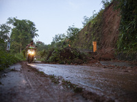 Residents on motorbikes cross a road section covered by landslide material after a flash flood and landslide hit Mekarbuana village, Karawan...