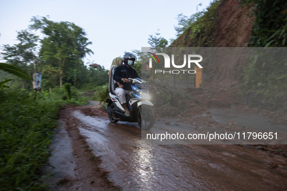 Residents on motorbikes cross a road section covered by landslide material after a flash flood and landslide hit Mekarbuana village, Karawan...