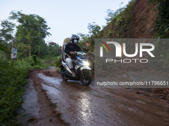 Residents on motorbikes cross a road section covered by landslide material after a flash flood and landslide hit Mekarbuana village, Karawan...