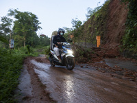 Residents on motorbikes cross a road section covered by landslide material after a flash flood and landslide hit Mekarbuana village, Karawan...