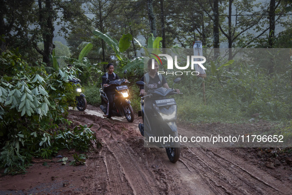 Residents on motorbikes cross a road section covered by landslide material after a flash flood and landslide hit Mekarbuana village, Karawan...