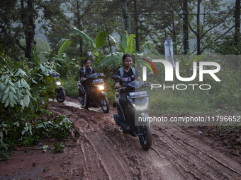 Residents on motorbikes cross a road section covered by landslide material after a flash flood and landslide hit Mekarbuana village, Karawan...