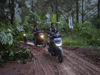 Residents on motorbikes cross a road section covered by landslide material after a flash flood and landslide hit Mekarbuana village, Karawan...