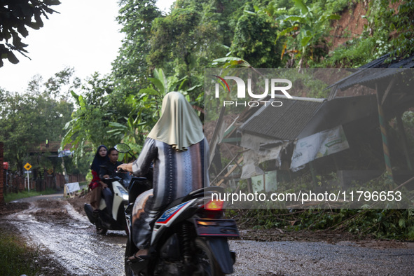 Residents on motorbikes cross a road section covered by landslide material after a flash flood and landslide hit Mekarbuana village, Karawan...