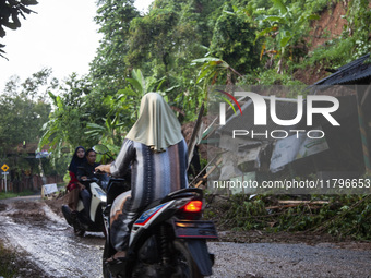 Residents on motorbikes cross a road section covered by landslide material after a flash flood and landslide hit Mekarbuana village, Karawan...