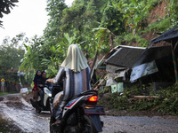 Residents on motorbikes cross a road section covered by landslide material after a flash flood and landslide hit Mekarbuana village, Karawan...