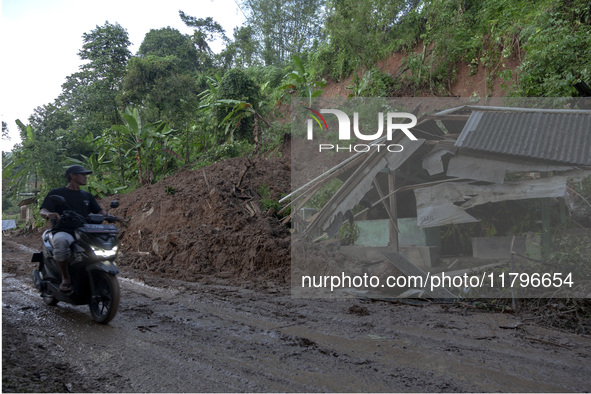 Residents on motorbikes cross a road section covered by landslide material after a flash flood and landslide hit Mekarbuana village, Karawan...