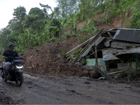 Residents on motorbikes cross a road section covered by landslide material after a flash flood and landslide hit Mekarbuana village, Karawan...