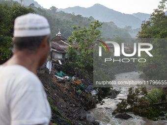 A resident watches damaged houses and fallen trees from a bridge after a flash flood and landslide hit Mekarbuana village, Karawang district...