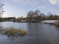 The lake and a wooden building in front of the forest in Park Meerland. First winter weather of the season with snow hit the Netherlands. Lo...