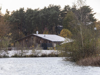 The lake and a wooden building in front of the forest in Park Meerland. First winter weather of the season with snow hit the Netherlands. Lo...