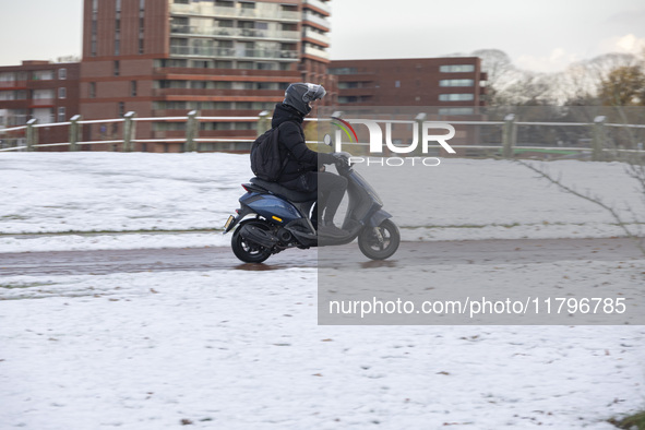 A young person on a motorcycle in the snowy road. First winter weather of the season with snow hit the Netherlands. Low temperatures with we...