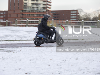 A young person on a motorcycle in the snowy road. First winter weather of the season with snow hit the Netherlands. Low temperatures with we...