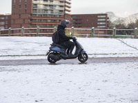 A young person on a motorcycle in the snowy road. First winter weather of the season with snow hit the Netherlands. Low temperatures with we...