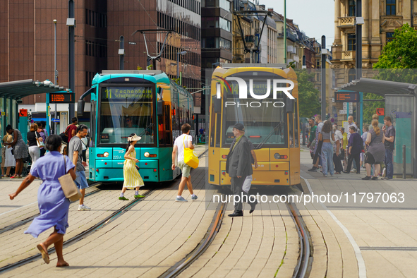 A woman runs to catch the tram at a bustling tram stop in Frankfurt am Main, Germany, on August 15, 2023. Two brightly colored trams, turquo...