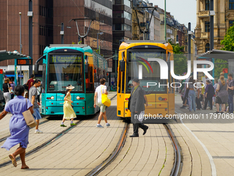 A woman runs to catch the tram at a bustling tram stop in Frankfurt am Main, Germany, on August 15, 2023. Two brightly colored trams, turquo...