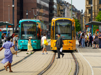 A woman runs to catch the tram at a bustling tram stop in Frankfurt am Main, Germany, on August 15, 2023. Two brightly colored trams, turquo...