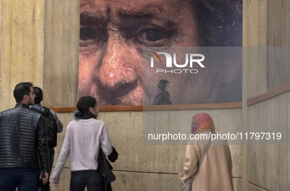 Young Iranian people walk under a copy of a detail of a self-portrait by Rembrandt (1659), the Irish painter and printmaker, while visiting...