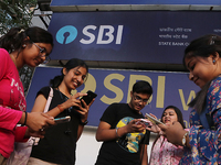 An Indian onlooker checks her mobile phone while watching share prices in front of a branch of State Bank of India Wealth Management in Kolk...