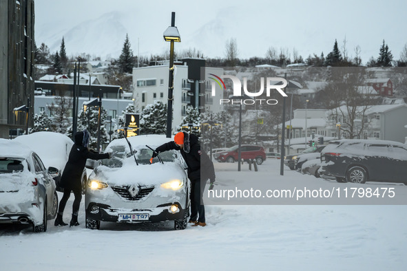 Two people clear snow from their cars in a parking lot in Akureyri, Iceland, on November 20, 2024. 