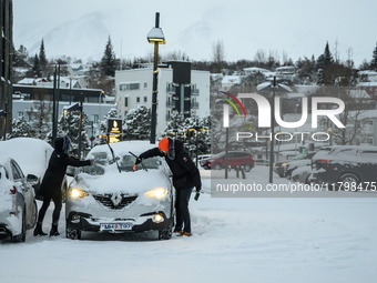 Two people clear snow from their cars in a parking lot in Akureyri, Iceland, on November 20, 2024. (