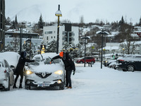 Two people clear snow from their cars in a parking lot in Akureyri, Iceland, on November 20, 2024. (