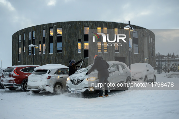 Two people clear snow from their cars in a parking lot in Akureyri, Iceland, on November 20, 2024. 