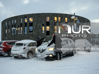 Two people clear snow from their cars in a parking lot in Akureyri, Iceland, on November 20, 2024. (