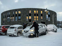 Two people clear snow from their cars in a parking lot in Akureyri, Iceland, on November 20, 2024. (