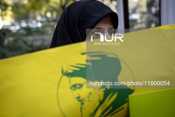 A veiled Iranian woman stands behind a yellow flag featuring a portrait of Lebanon's Hezbollah late leader, Hassan Nasrallah, who was killed...