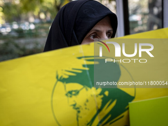 A veiled Iranian woman stands behind a yellow flag featuring a portrait of Lebanon's Hezbollah late leader, Hassan Nasrallah, who was killed...